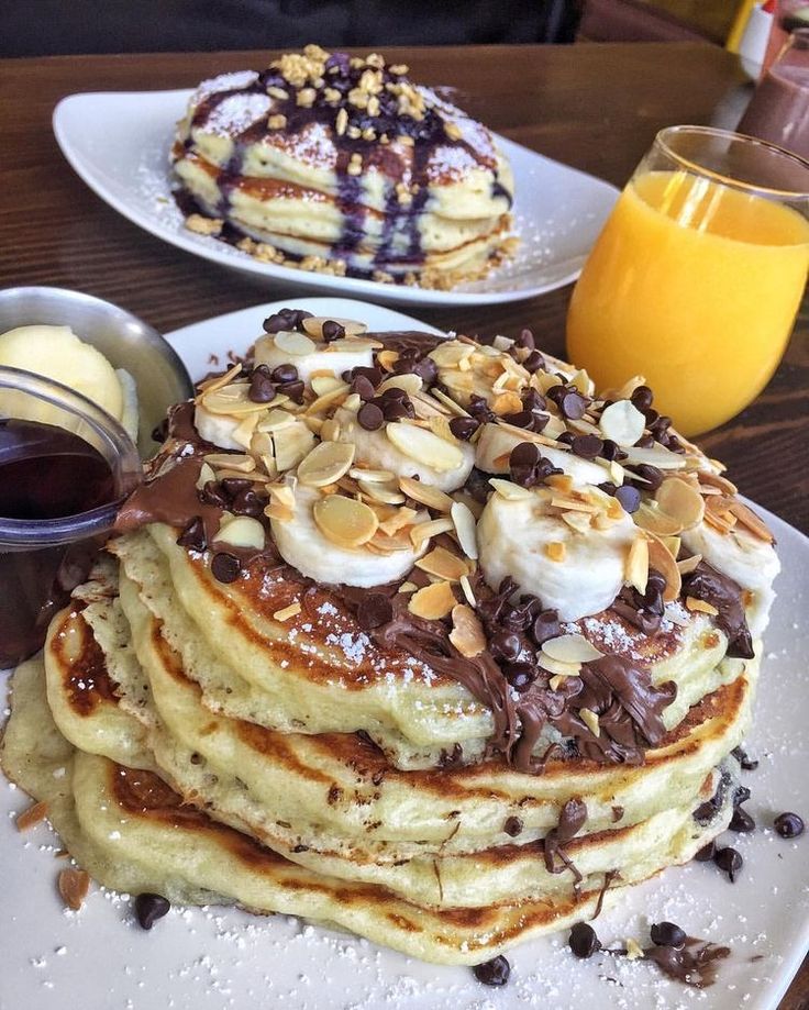 a stack of pancakes on a plate with chocolate sauce and nuts next to some orange juice