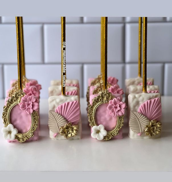 four pink and white candy bars with gold trimmings on top of a counter