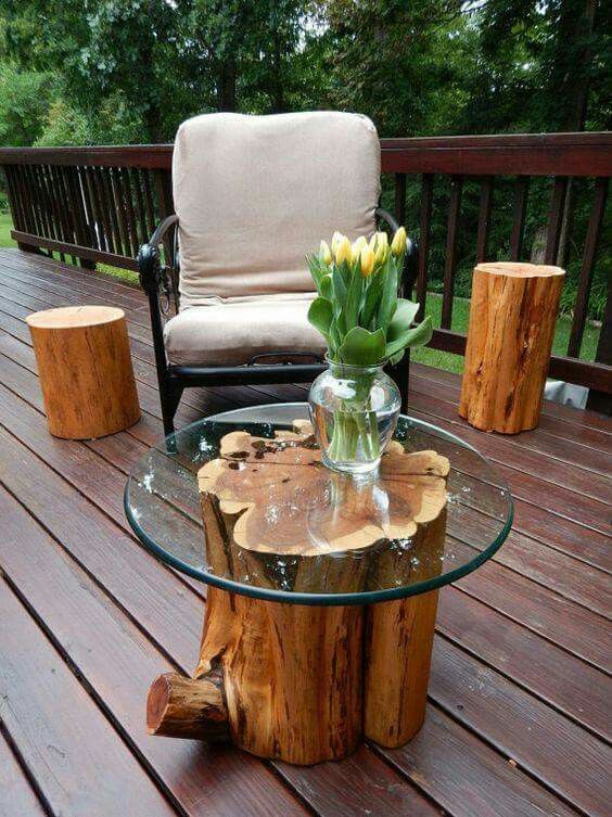 a glass table with flowers on it sitting on a wooden deck next to a chair