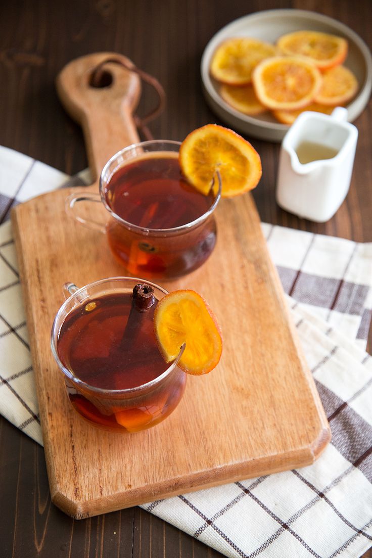 two glasses filled with liquid sitting on top of a cutting board next to sliced oranges