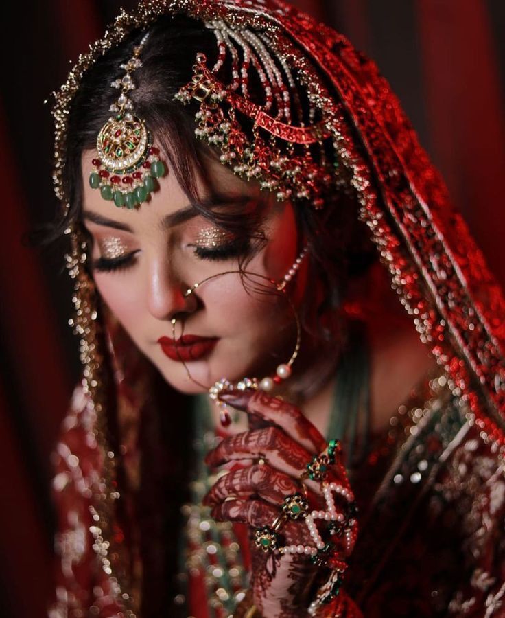 a woman in red and gold is dressed up for her wedding day, with jewelry on her face