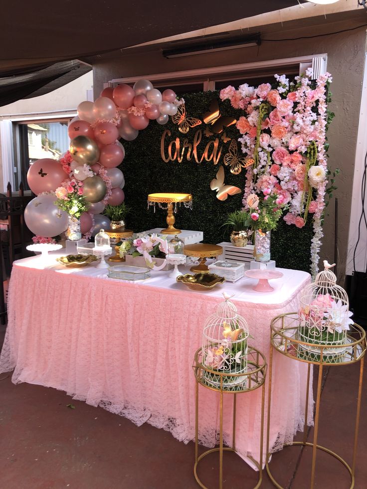 a table topped with lots of pink and gold balloons next to a wall covered in flowers