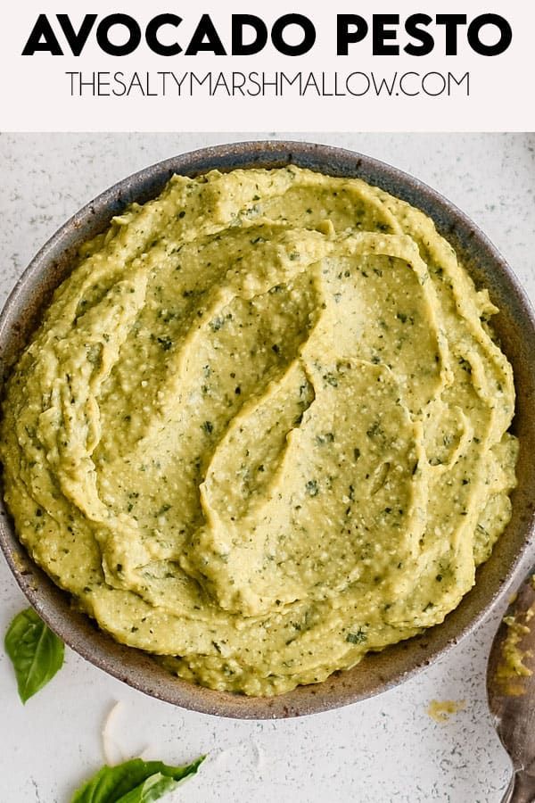 avocado pesto hummus in a bowl with basil leaves and garlic on the side