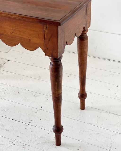 an old wooden table with scalloped legs on white wood flooring and walls in the background