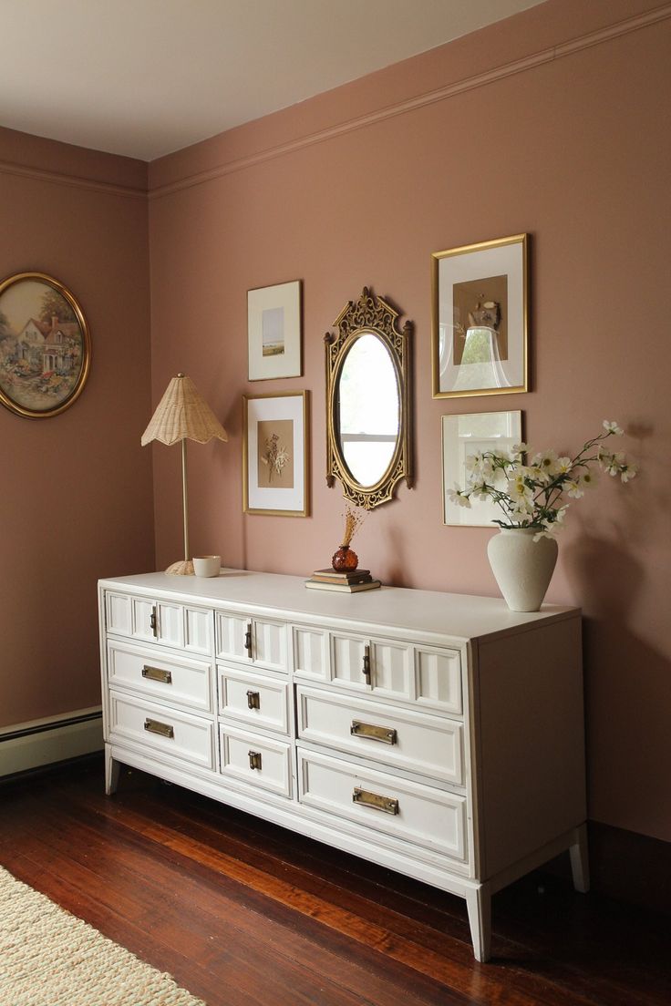 a white dresser sitting in a living room next to a wall with pictures on it