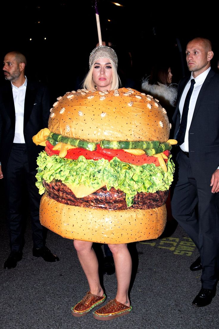 a woman in a giant hamburger costume is walking with a man behind her and an umbrella over her head