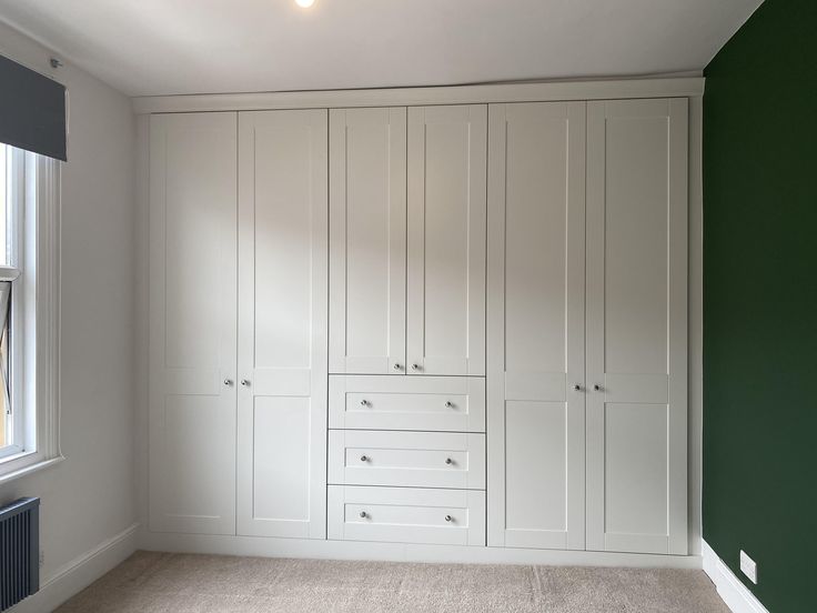 an empty room with green walls and white cabinets on the wall, next to a radiator