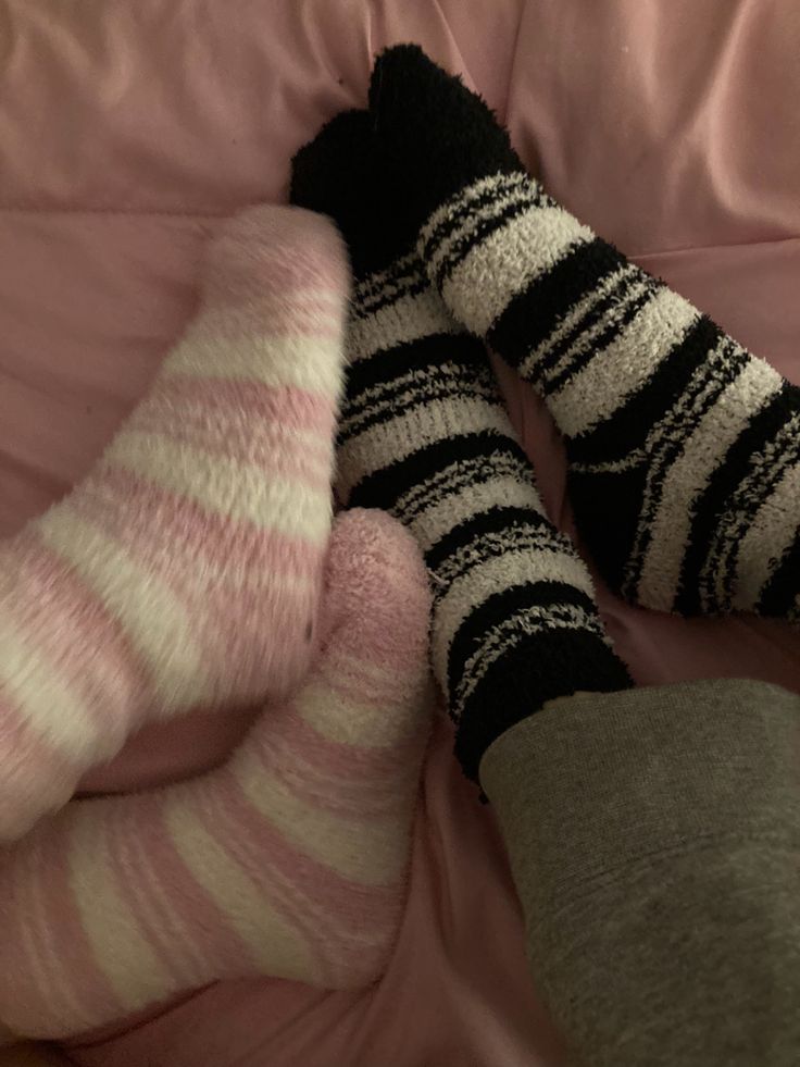 two pairs of socks laying on top of a pink bed sheet with the feet up