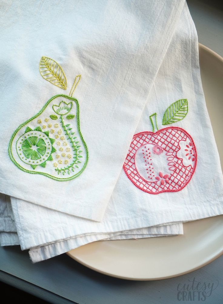 two tea towels with embroidered apples and pears on them are sitting on a plate