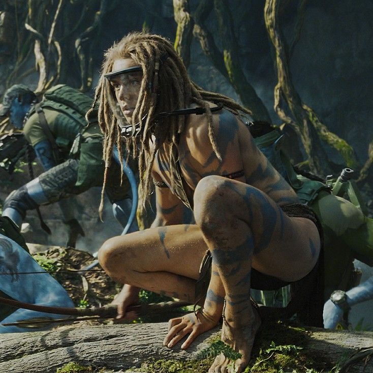 a woman with dreadlocks crouches on a rock in front of other people