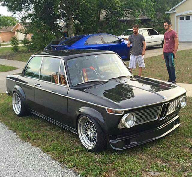 two men standing next to an old bmw