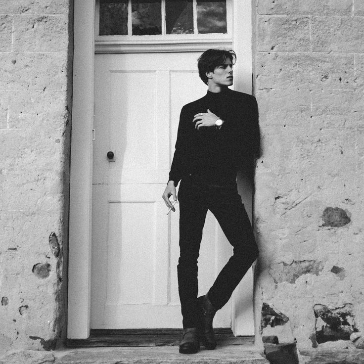 black and white photograph of a young man leaning against a door with his hands in his pockets