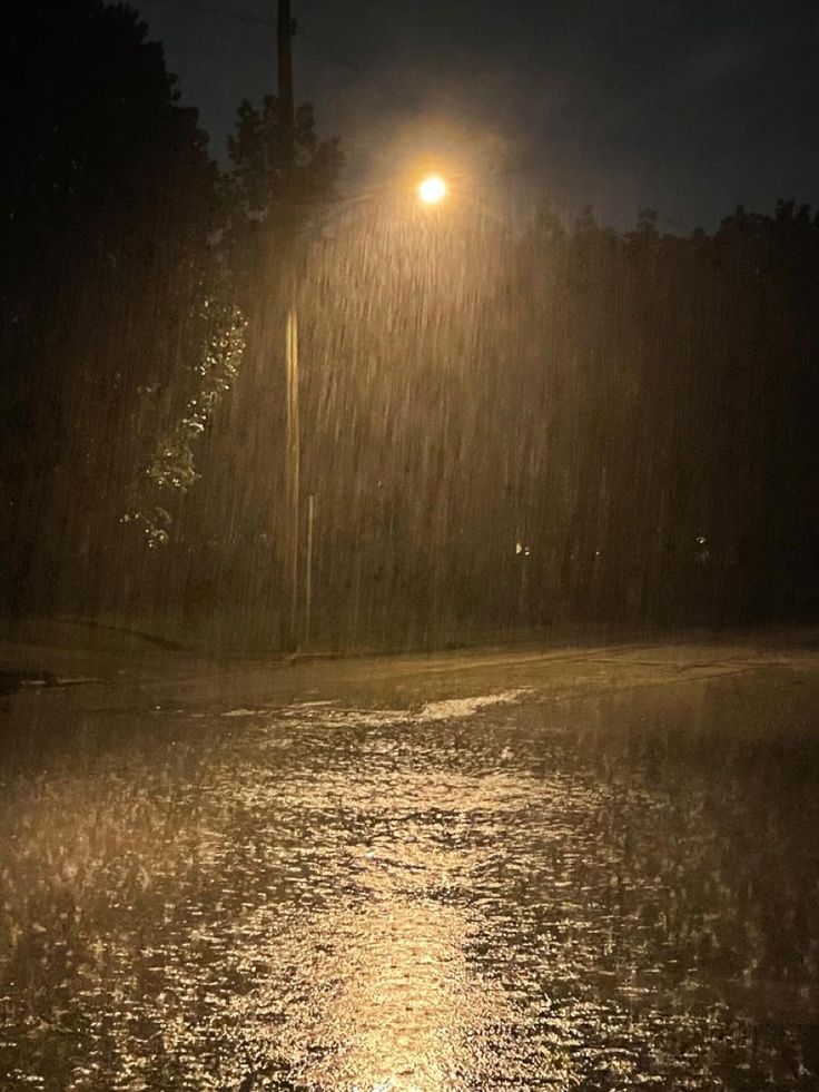 a street light shines brightly in the rain at night, as it rains down