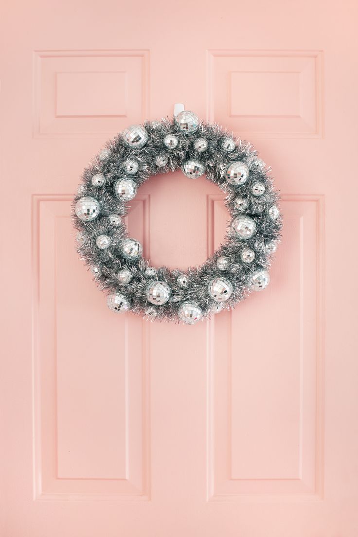 a christmas wreath on a pink door with silver ornaments hanging from it's side