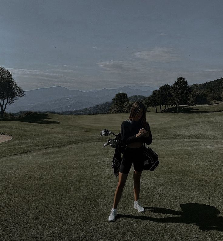 a woman standing on top of a lush green field next to a golf ball and bag