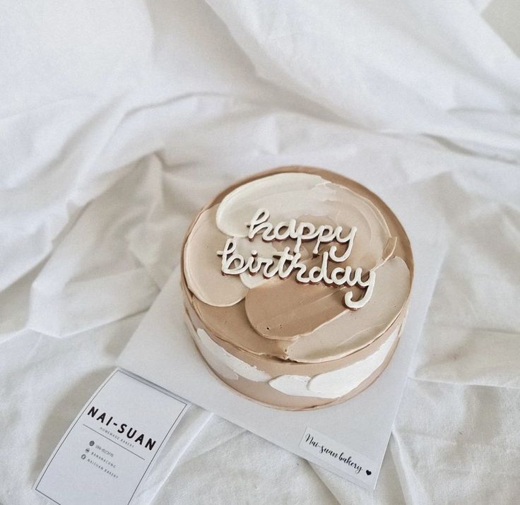 a birthday cake sitting on top of a white sheet covered bed next to a tag