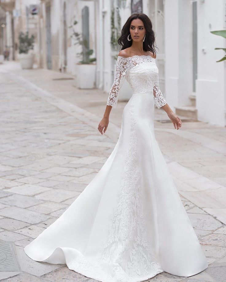 a woman in a white wedding dress standing on the street with her hand on her hip