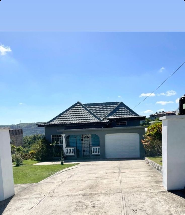 an empty driveway leading to a house with two garages on each side and a blue sky in the background