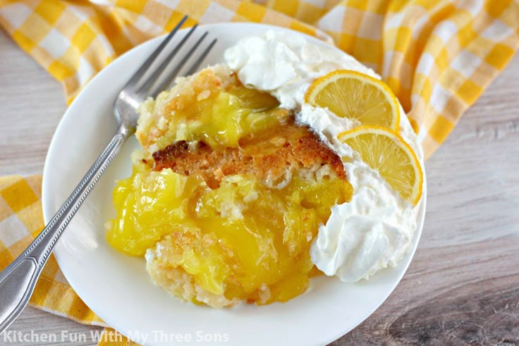 a white plate topped with lemon cobbler and whipped cream next to a fork on a yellow checkered napkin