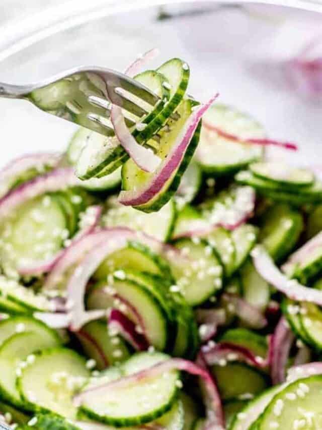 cucumber and onion salad in a glass bowl with a fork stuck into it