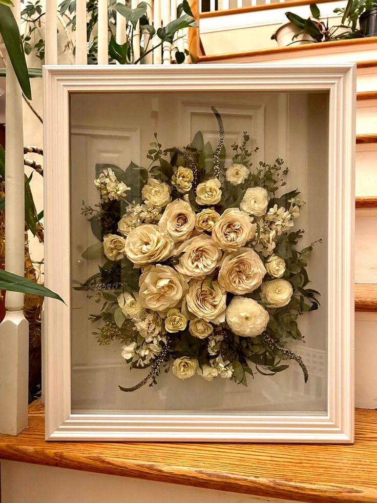 an arrangement of flowers is displayed in a white frame on the steps leading up to a stair case