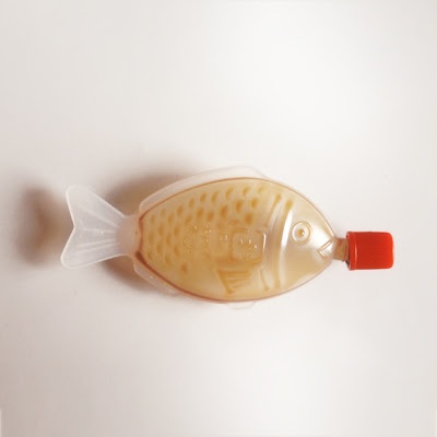 a plastic fish shaped bottle with a red cap on it's head sitting on a white surface