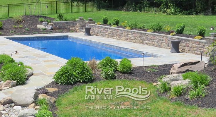 a pool surrounded by rocks and plants in the middle of a yard with a stone wall