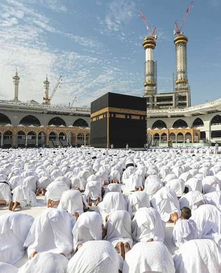 many people in white robes are praying at the ka'bah, with two large towers in the background