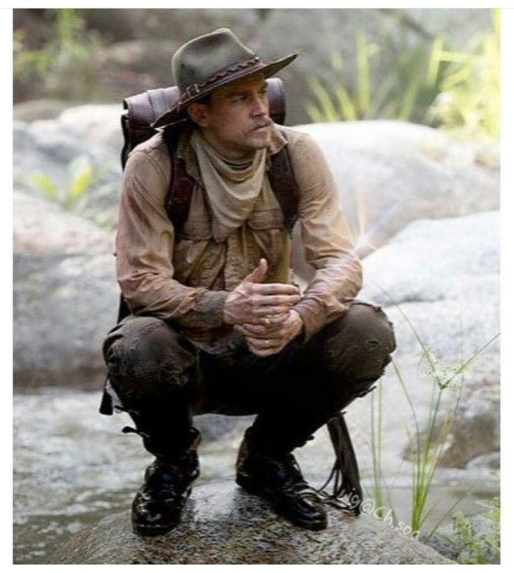 a man with a hat and backpack is sitting on a rock in the water while holding his hands together