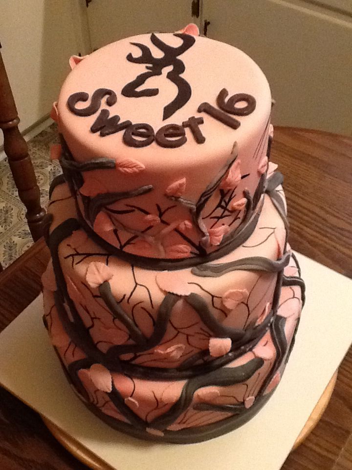 a three tiered cake decorated with pink frosting and black icing on a wooden table