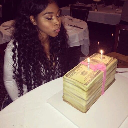 a woman sitting in front of a cake with money stacked on it and lit candles