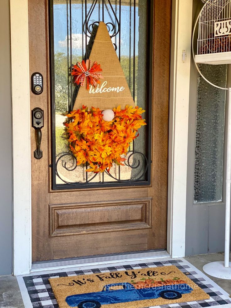 a welcome mat on the front door with an orange and yellow wreath hanging from it