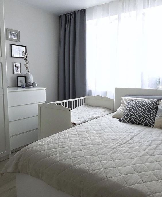 a white bed sitting in a bedroom next to a window with curtains on the windowsill