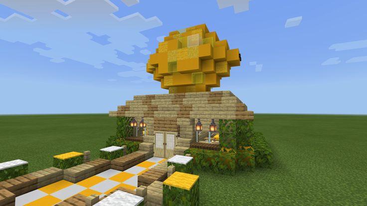 a small house made out of blocks in the middle of a grassy area with yellow and white tables