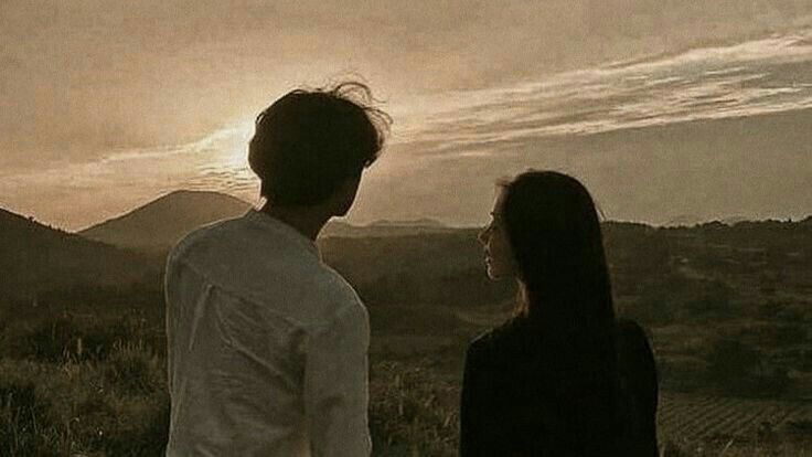 a man and woman standing in front of a sunset