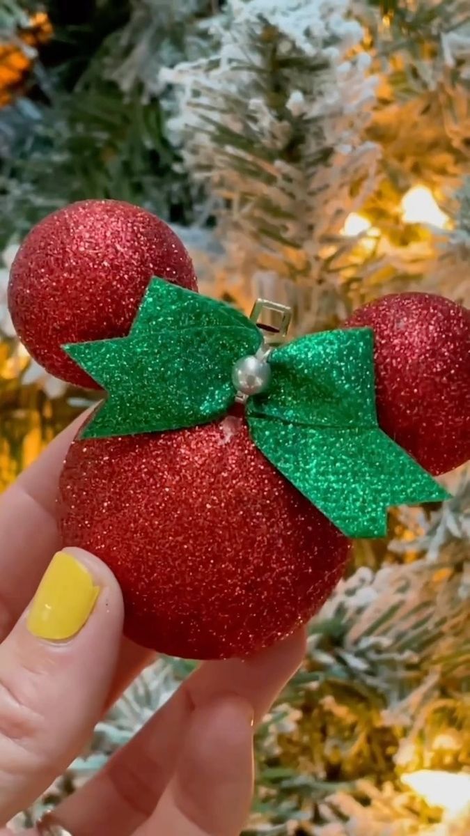 someone is holding up a red ornament with a green bow