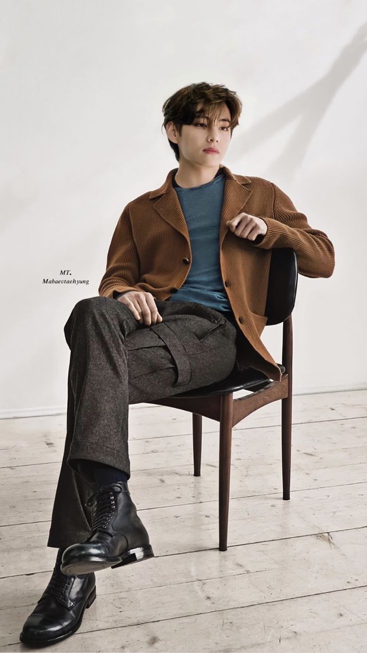 a man sitting on top of a wooden chair wearing a brown coat and black shoes