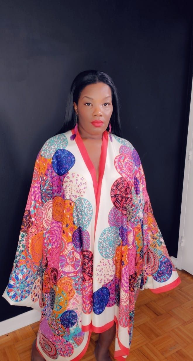 a woman standing in front of a black wall wearing an orange and pink shawl