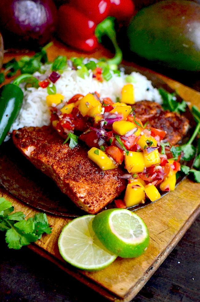 fish with mango salsa and rice on a wooden cutting board next to lime wedges