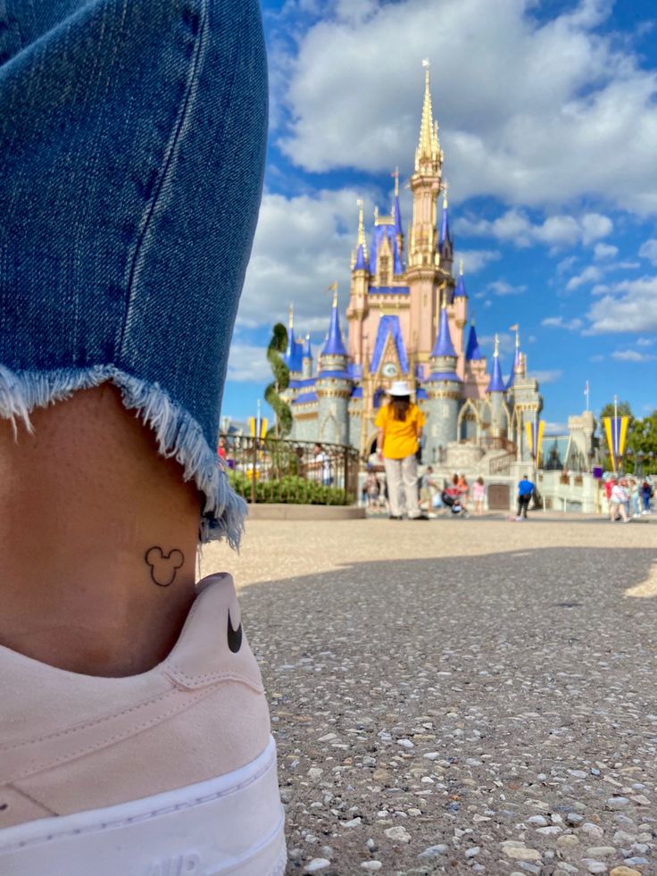 a person's foot with a small heart tattoo on their left ankle in front of a castle