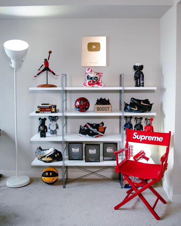 a red chair sitting in front of a white book shelf filled with sports memorabilia and shoes