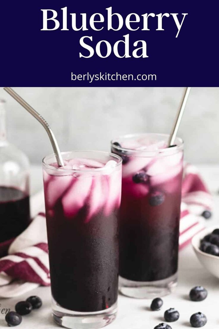 two glasses filled with blueberry soda sitting on top of a table next to berries