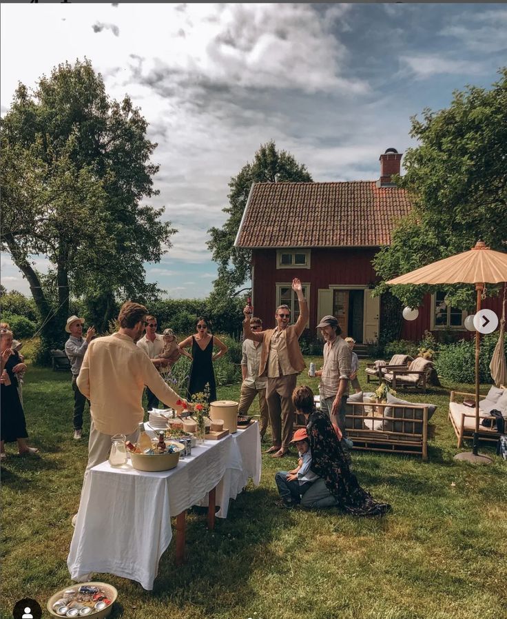 a group of people standing around a table with food and drinks on it in front of a house