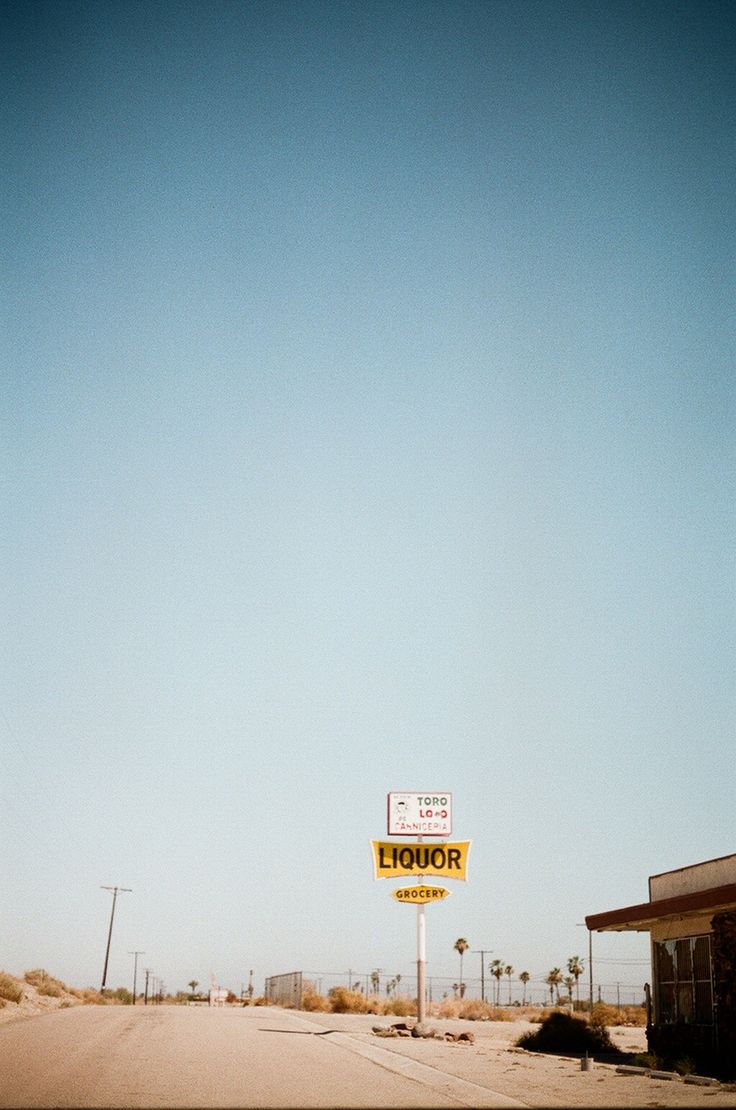 a yellow sign sitting on the side of a road in front of a building and palm trees