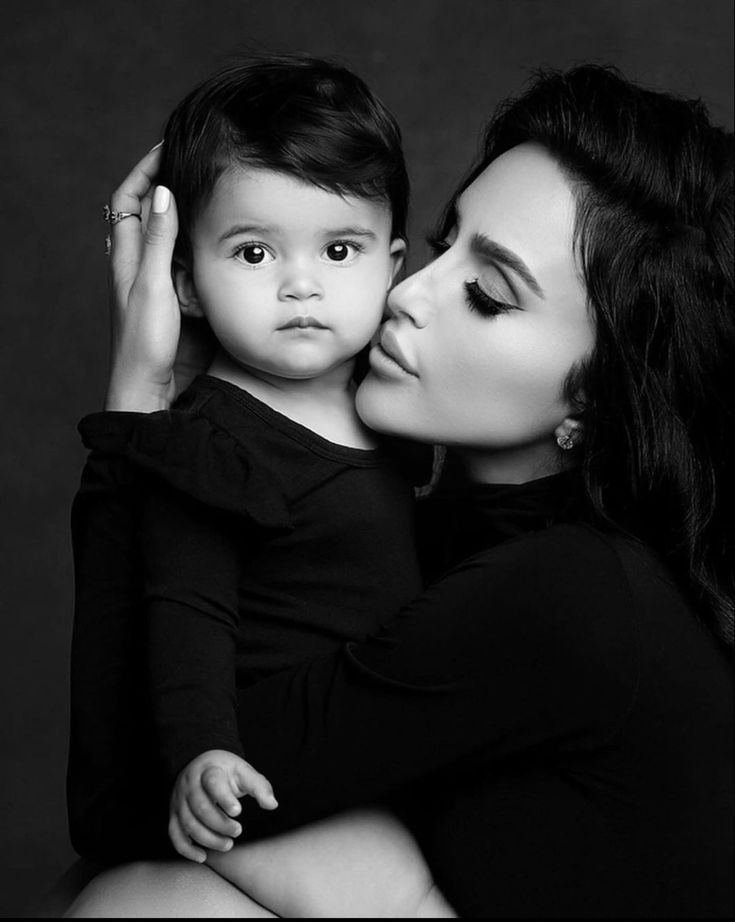 a woman kissing a small child with her face close to her chest, in black and white