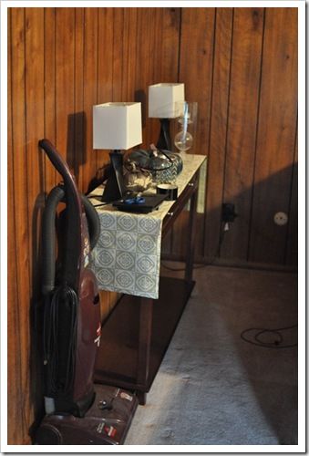 a room with wood paneling and an ironing board next to a lamp on a table