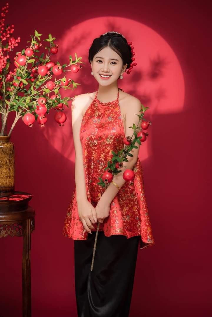 a woman standing in front of a red wall holding a plant and smiling at the camera