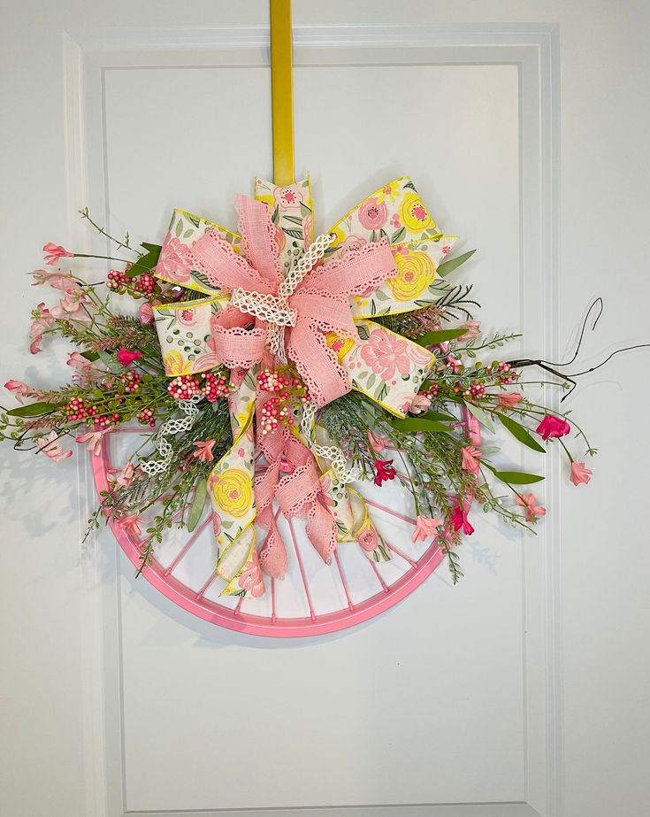 a wreath with flowers and ribbons hanging on a door hanger in front of a white door