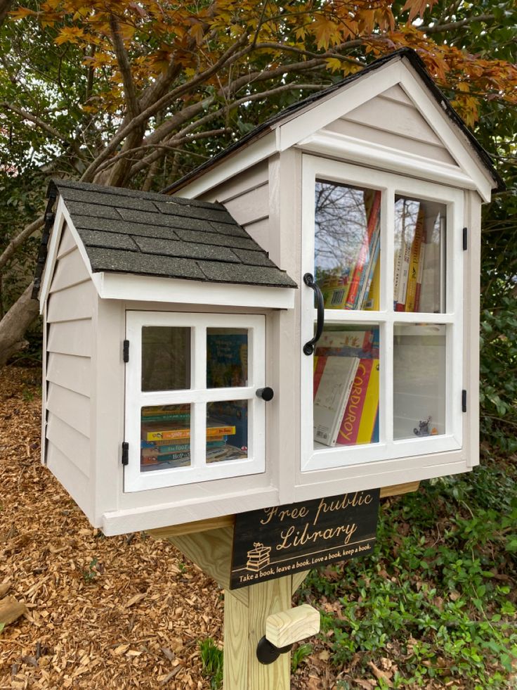 a little library with lots of books in it's windows and some leaves on the ground