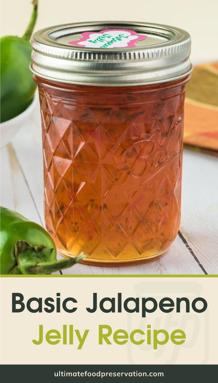 a glass jar filled with jelly sitting on top of a table next to green peppers